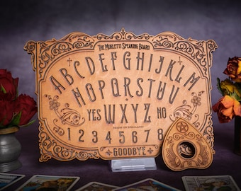May include: A wooden Ouija board with a planchette in the shape of a teardrop. The board features the alphabet, numbers 1-8, "yes", "no", and "goodbye". The board is decorated with intricate carvings and a floral design.