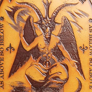 May include: A brown leather plaque with a raised image of a horned figure with wings. The figure is sitting with its legs crossed and has a star on its forehead. The text "AS ABOVE SO BELOW" is written on the plaque.