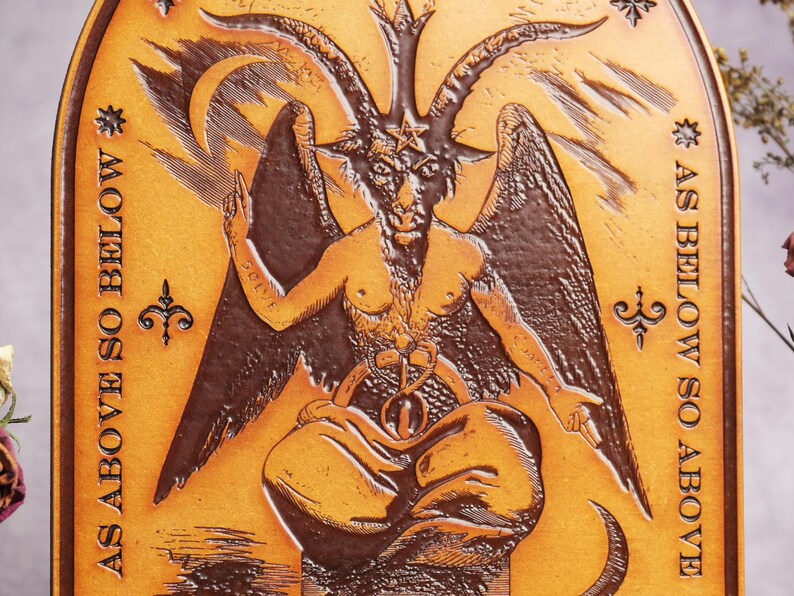 May include: A brown leather plaque with a raised image of a horned figure with wings. The figure is sitting with its legs crossed and has a star on its forehead. The text "AS ABOVE SO BELOW" is written on the plaque.