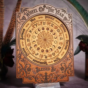 May include: A wooden wheel of the year with a circular design featuring the eight sabbats of the Wiccan calendar. The wheel is decorated with intricate carvings and the text "Wheel of the Year" and "Blessed Be".