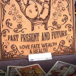 May include: A brown leather board with a hand drawn on it. The hand has lines drawn on it, and the text "PAST PRESENT AND FUTURE LOVE FATE WEALTH & HEALTH" is written below the hand.