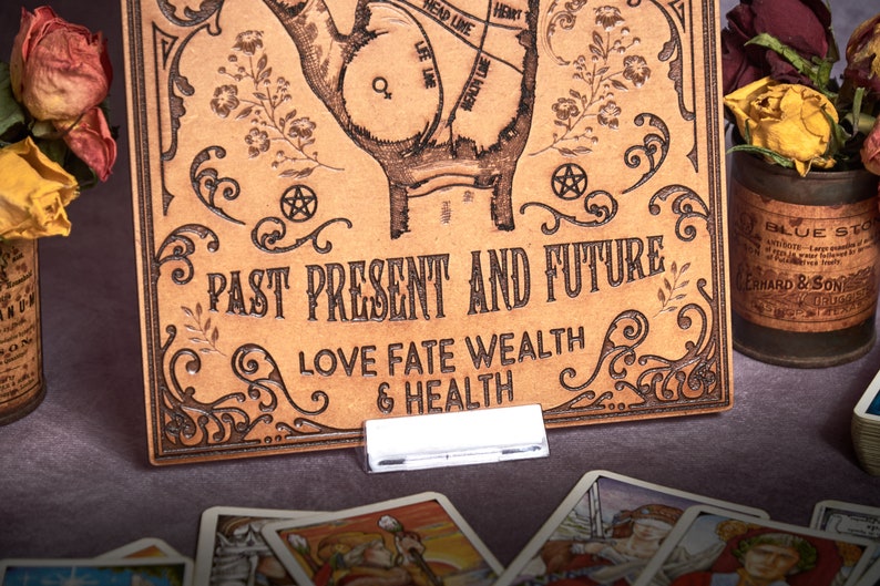 May include: A brown leather board with a hand drawn on it. The hand has lines drawn on it, and the text "PAST PRESENT AND FUTURE LOVE FATE WEALTH & HEALTH" is written below the hand.