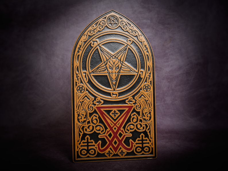 May include: A black and gold leather plaque featuring a pentagram and other occult symbols. The pentagram has a goat's head in the centre.