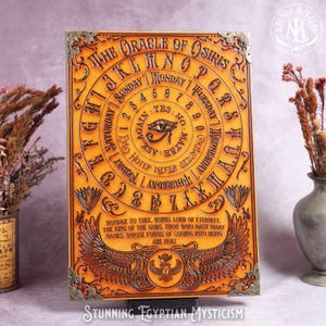 May include: An orange-toned, rectangular Oracle of Osiris board with embossed lettering and symbols. The board features a central eye symbol, a circular alphabet, and the text "The Oracle of Osiris". Decorative metal corner pieces add detail.