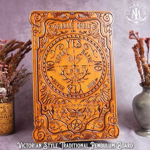 May include: A rectangular, tan-colored Victorian-style pendulum board with ornate carvings. The board features the text "ORACLE ORBIS" at the top, a central compass design with "YES," "NO," and "MAYBE" indicators, and the phrase "AS ABOVE SO BELOW."