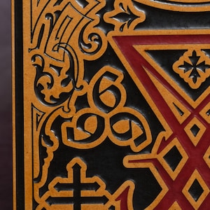 May include: Close-up of a black leather journal with a gold and red embossed design. The design features a cross, a star, and a geometric pattern.