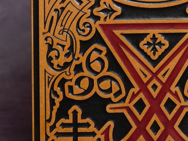 May include: Close-up of a black leather journal with a gold and red embossed design. The design features a cross, a star, and a geometric pattern.