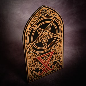 May include: A black and gold wooden plaque featuring a pentagram with a goat's head inside. The plaque also has a red inverted pentagram with the word "666" at the bottom.