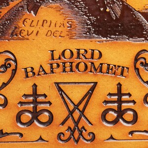 May include: A close-up of a leather-bound book with the words "LORD BAPHOMET" embossed in gold lettering. The book also features two symbols, a pentagram and a cross with an infinity symbol.