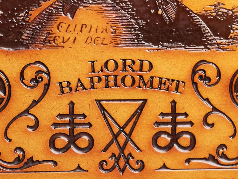 May include: A close-up of a leather-bound book with the words "LORD BAPHOMET" embossed in gold lettering. The book also features two symbols, a pentagram and a cross with an infinity symbol.