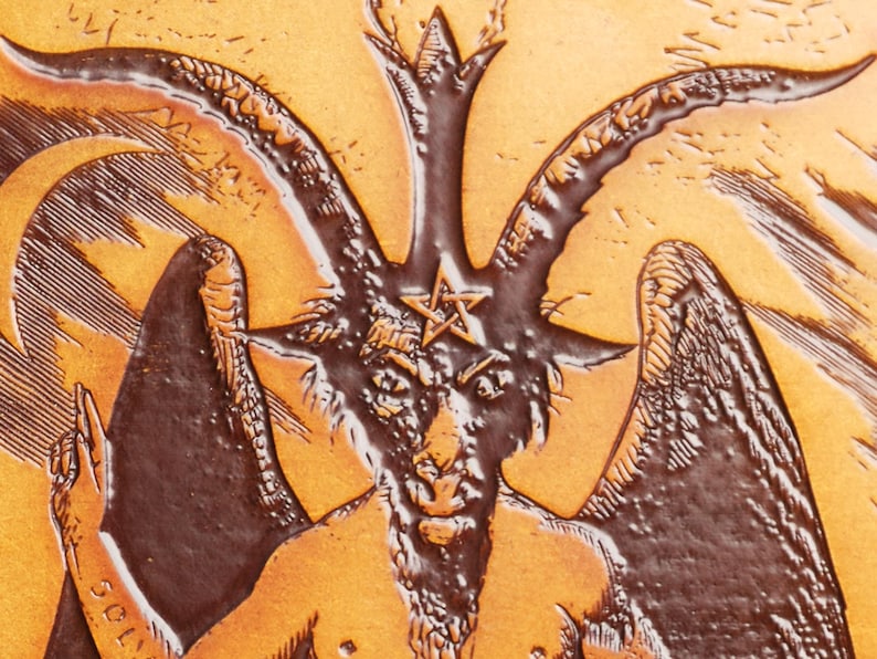 May include: A brown leather embossed image of a goat with horns and wings. The goat has a pentagram on its forehead and a beard. The background is a light brown color.