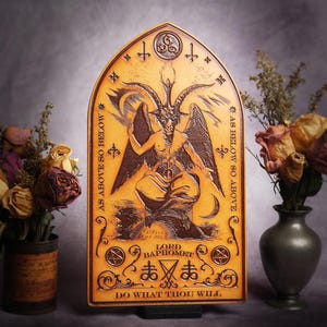 May include: A brown wooden plaque with a gold-coloured design. The plaque features a depiction of a horned figure with wings, surrounded by symbols and text. The text reads "As Above So Below", "As Below So Above", "Lord Baphomet", "Do What Thou Wilt", and "まぁ".