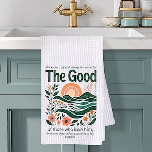 May include: White waffle-weave kitchen towel with a floral and landscape design. The towel features the text "The Good" in green, with a quote about God's work. The design includes orange flowers, green leaves, and a sunset.