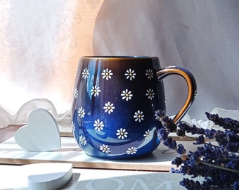 May include: A blue and brown ceramic mug with a white daisy pattern. The mug has a rounded shape and a handle.