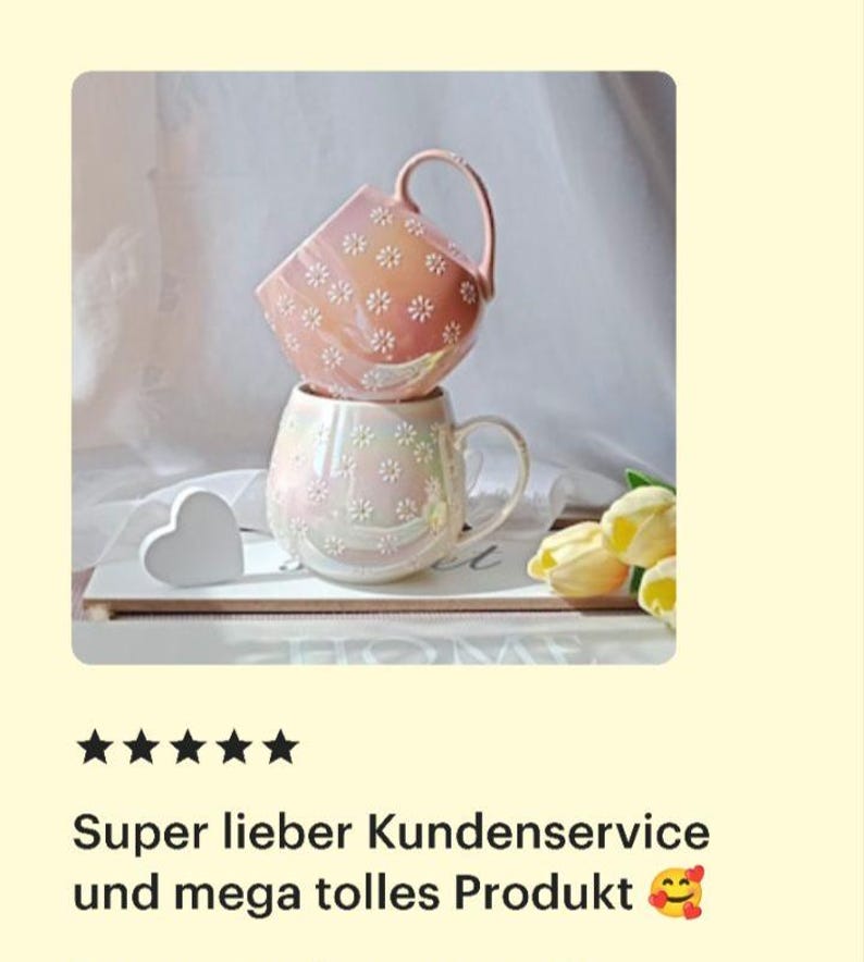 May include: Two pink ceramic mugs with a daisy pattern. The top mug is a lighter shade of pink and the bottom mug is a slightly darker shade of pink. The mugs are stacked on top of each other and are sitting on a wooden surface.