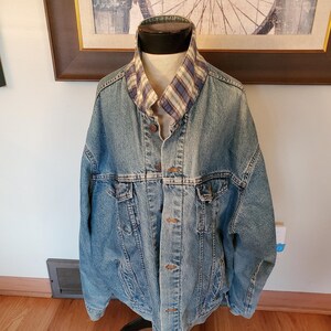 May include: A light blue denim jacket with a plaid flannel collar. The jacket has a button closure and two front pockets.