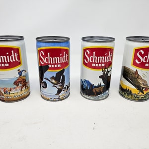 May include: Four vintage aluminum cans of Schmidt Beer. Each can features a different image of wildlife, including a cowboy riding a horse, a pair of geese flying, a deer, and a fish being caught by a bear. The cans have the text "Schmidt Beer" printed on them.