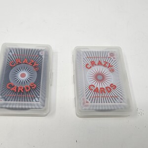 May include: Two clear plastic boxes containing decks of playing cards. The cards have a black and white design with the words "CRAZY CARDS" in red.