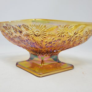 May include: A vintage iridescent amber glass pedestal bowl with a floral design. The bowl has a square base and a rounded top.