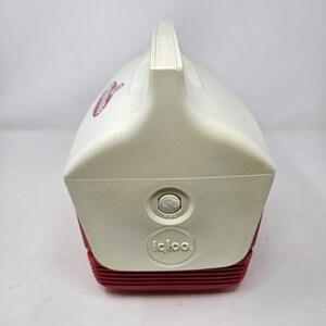 Puede incluir: Nevera Igloo blanca y roja con un bot&oacute;n pulsador y el texto "PUSH" en el lateral. La nevera tiene un asa en la parte superior y el logotipo de Igloo en la parte delantera.