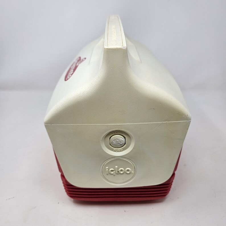 Puede incluir: Nevera Igloo blanca y roja con un bot&oacute;n pulsador y el texto "PUSH" en el lateral. La nevera tiene un asa en la parte superior y el logotipo de Igloo en la parte delantera.