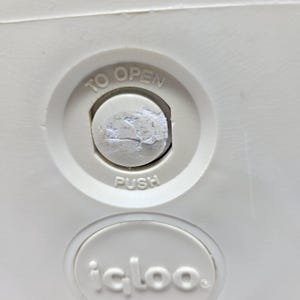 Puede incluir: Primer plano de una nevera blanca con un bot&oacute;n redondo blanco que dice "TO OPEN" y "PUSH". La nevera tiene una etiqueta blanca que dice "igloo."