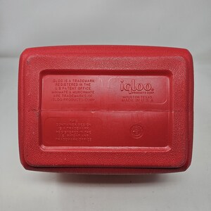 Puede incluir: Enfriador rojo Igloo con el texto "igloo. Products Corp. Houston Texas Made in USA" y "GLOO is a trademark registered in the U.S. Patent Office. WIKIVATE & MUNCHMATE are trademarks of GLOO PRODUCTS CORP." en la parte inferior.