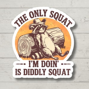 May include: A sticker with a raccoon wearing a cowboy hat and sitting on a log. The text reads "The only squat I'm doin' is diddly squat."