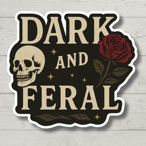 May include: A die-cut sticker with a black background featuring the text DARK AND FERAL in a cream-colored serif font. The design includes a beige human skull on the left, a deep red rose with green leaves on the right, and small gold stars.