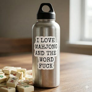 May include: A stainless steel water bottle with a black cap and the text "I LOVE MAHJONG AND THE WORD FUCK" in a white sticker. Mahjong tiles are in the foreground.