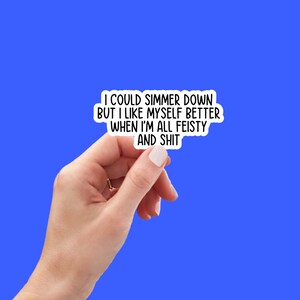 Op de afbeelding: Witte sticker met zwarte tekst die luidt: "Ik zou kunnen kalmeren, maar ik vind mezelf leuker als ik vol energie en eigenwijs ben."