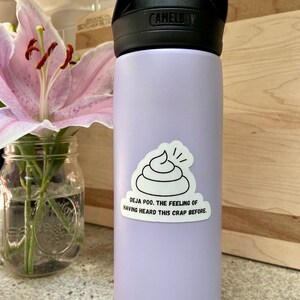 May include: A lavender water bottle with a black lid and handle. A white sticker with a black outline of a pile of poop and the text "Deja poo. The feeling of having heard this crap before." is on the bottle.