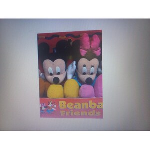 May include: A boxed set of plush toys featuring Mickey and Minnie Mouse. Mickey has black ears and a yellow body, while Minnie has a pink bow and a pink and purple body. The box reads "Beanba Friends".