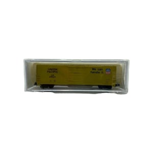 Pode incluir: Um vagão de trem modelo Union Pacific amarelo em uma caixa de plástico transparente. O vagão tem rodas pretas e o texto "Union Pacific" e "We can handle it." O modelo é uma réplica em miniatura de um vagão de carga.