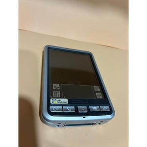 Può includere: Dispositivo portatile argentato con touchscreen. Il dispositivo ha una forma rettangolare con angoli arrotondati e uno schermo nero. Ha diversi pulsanti e icone. Il testo "High Resolution" è visibile sul dispositivo.