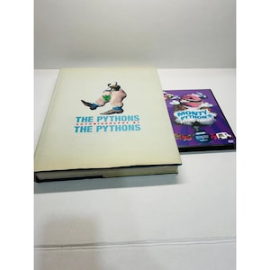 Op de afbeelding: Een hardcover boek getiteld The Pythons Autobiography by The Pythons met een afbeelding van een persoon in een pak en een oversized broek op de kaft, naast een dvd-hoesje voor Monty Python's Flying Circus met een paarse achtergrond en wolken.