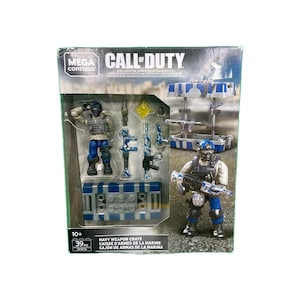 May include: A Mega Construx Call of Duty Navy Weapon Crate set. The box features two soldier figures, weapons, and a crate. The set includes 39 pieces. The box has a blue and white color scheme.