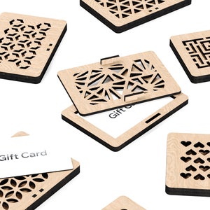 May include: A set of six wooden gift card holders with intricate laser-cut designs. Each holder features a different geometric pattern, including hearts, stars, and geometric shapes. The holders are made of light brown wood with black edges and have a slot for a gift card. The text "Gift Card" is visible on one of the holders.