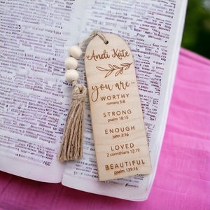 May include: Wooden bookmark with the names "Andi Kate" and the text "You are - Worthy, Strong, Enough, Loved, Beautiful" with bible verses listed below each word. The bookmark has a brown tassel.