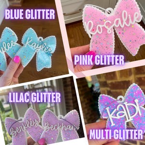 Può includere: Una collezione di ornamenti a forma di fiocco con superfici glitterate in blu, rosa, lilla e multicolore. Ogni ornamento mostra un nome in corsivo bianco, inclusi Kaylee, Rosalie, Berkley, Beckham e Kadi, con un occhiello per appenderlo.