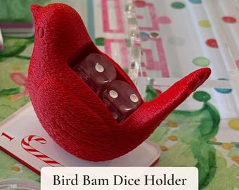 May include: A bright red 3D-printed bird-shaped dice holder with a hollow center containing two translucent red dice. The object features a textured surface and is labeled with the text Bird Bam Dice Holder for Mahjong Dice Included.