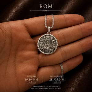 A silver pendant necklace featuring a detailed circular charm. The charm depicts a woman with long hair, flanked by two stylized animal figures. The pendant hangs from a delicate silver chain, creating an elegant accessory.