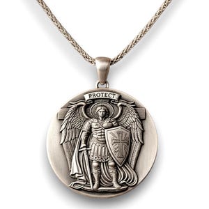 May include: Silver pendant necklace. The pendant features a detailed depiction of an angel with wings, holding a sword and shield. The word "PROTECT" is inscribed above the angel. The pendant hangs from a silver chain.