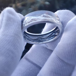 May include: A silver ring with a clear resin inlay featuring a mountain scene. The ring is marked with "S 925" on the inside band.