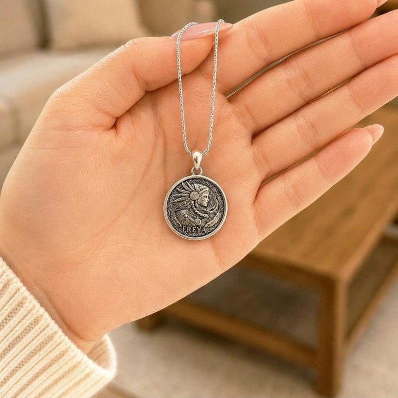 May include: A silver-toned necklace featuring a circular pendant with an embossed profile of a figure wearing a feathered headdress. The word FREYA is inscribed at the bottom of the coin-shaped charm, which hangs from a delicate silver-toned chain.