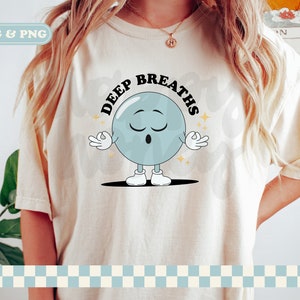 May include: A white t-shirt with a blue cartoon character meditating with the text "Deep Breaths" in black.