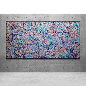 May include: Abstract expressionist painting with a black frame. The artwork features a chaotic arrangement of blue, red, and white paint splatters on a light background. The painting is displayed on a concrete wall.