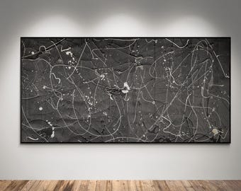 May include: Abstract black and white painting in a rectangular black frame. The artwork features a textured, dark background with white paint splatters and linear strokes, creating a dynamic and expressive composition. The painting is displayed on a white wall.