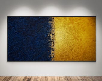 May include: Abstract wall art featuring a textured, rectangular canvas divided vertically. The left side is a deep navy blue, while the right side is a shimmering gold. The artwork is framed in black and mounted on a white wall.