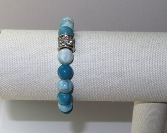 May include: A blue and white gemstone bracelet with a silver and crystal accent. The bracelet is displayed on a white fabric stand.